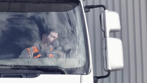 Truck driver sitting in parked truck looking in mirror